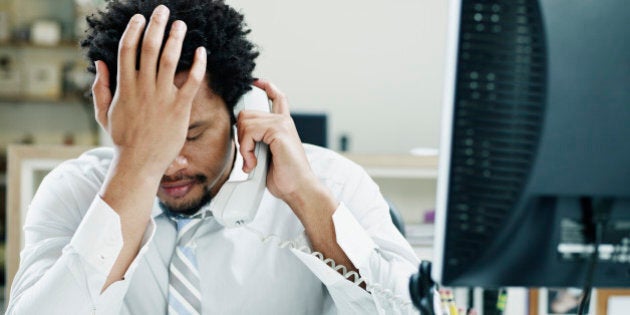 Businessman on phone at desk in office with hand on forehead