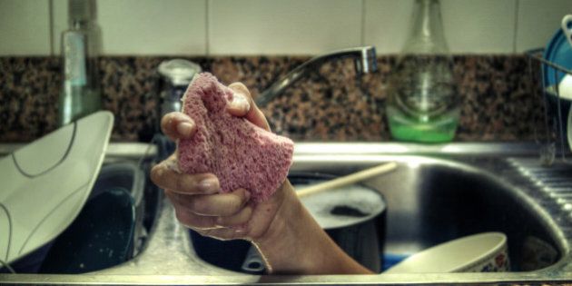 Surreal arm rising up from kitchen sink, holding pink sponge to wash dishes. Dirty dishes in sink. Natural lighting.