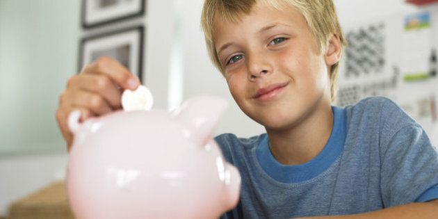 Boy (7-9) putting coin into piggy bank, smiling, portrait