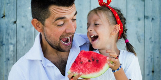 happy father playing with cute little daughter holding watermelon