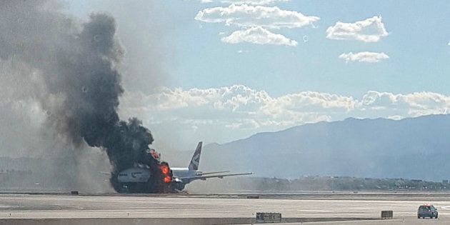 In this photo taken from the view of a plane window, smoke billows out from a plane that caught fire at McCarren International Airport, Tuesday, Sept. 8, 2015, in Las Vegas. An engine on the British Airways plane caught fire before takeoff, forcing passengers to escape on emergency slides. (Eric Hays via AP) MANDATORY CREDIT