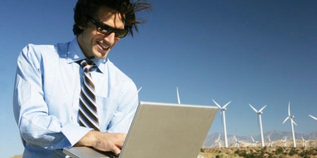Young businessman using laptop near wind turbines.