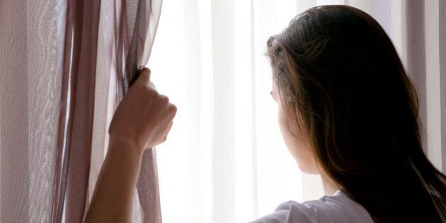 rear view of teenage girl looking through curtain
