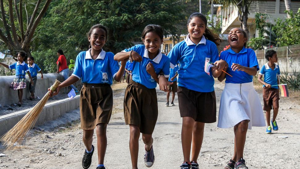 Four school girls laugh and play as they make their way down to the Tour de Timor 2016 finish line. Baucau, Timor-Leste.