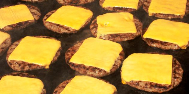 Beef hamburgers cooking on barbecue with melting cheese slice on top.