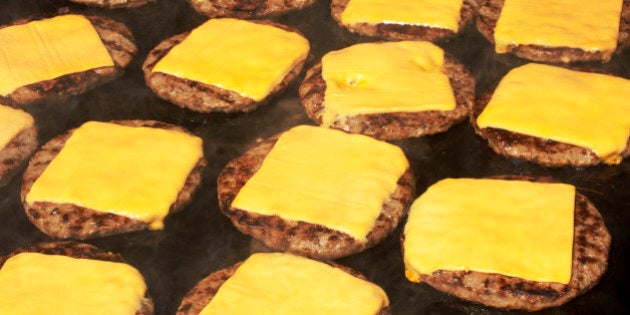 Beef hamburgers cooking on barbecue with melting cheese slice on top.