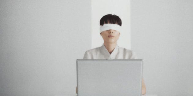 Blindfolded woman sitting behind laptop