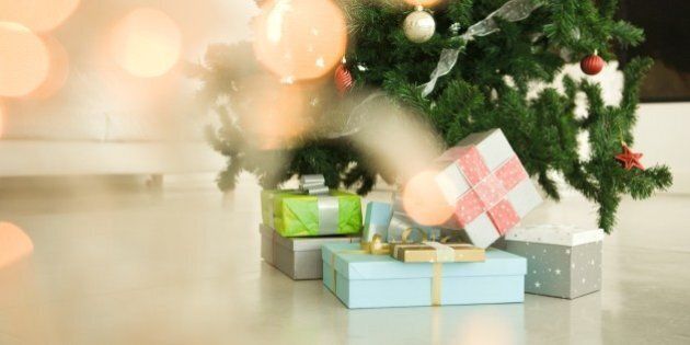 Christmas presents stacked beneath Christmas tree, view through Christmas lights, selective focus