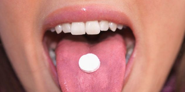 Young woman holding pill on tongue, close-up