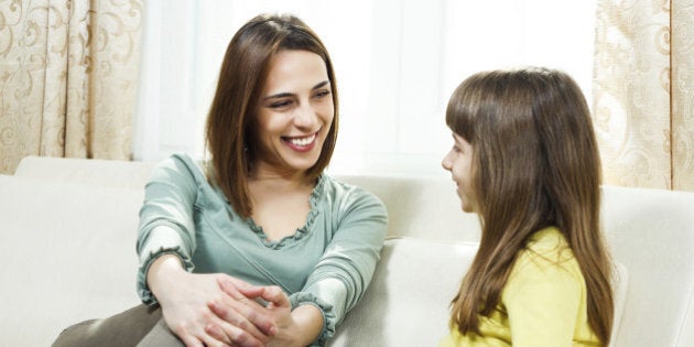 Mother and daughter sitting on sofa at their home and talking.