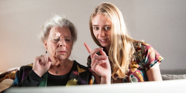 Senior woman and granddaughter sitting on sofa with laptop. The girl is teaching the grandmother how it works.