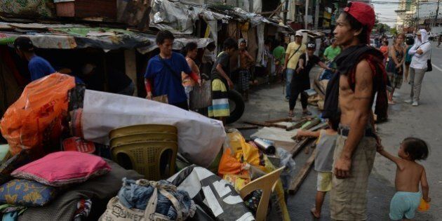 A father holds his children next to their belongings as he watches workers demolished their makeshift house erected along pedestrian lane on a street in Quezon City suburban Manila on September 29, 2015, as city officials intensified its campaign against illegal structures along pedestrian lanes and streets, blocking the flow of traffic. Traffic jams in the Philippine capital of 12 million have worsened in recent months, as the government rushed to build elevated tollways to accommodate the growing number of vehicles acquired amid a booming economy, but roughly one quarter of the nation's 100 million people live in poverty, which is defined as surviving on about one dollar a day. AFP PHOTO / TED ALJIBE (Photo credit should read TED ALJIBE/AFP/Getty Images)