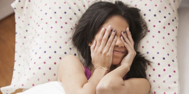 Hispanic teenage girl covering eyes in bed