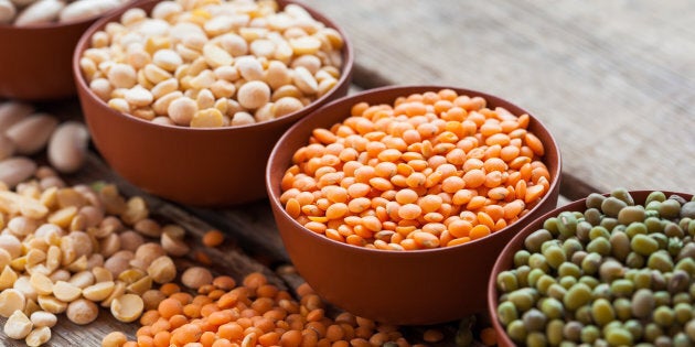 Bowls of cereal grains: red lentils, green mung, corn, beans and peas on wooden kitchen table. Selective focus.