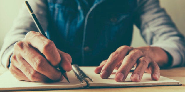 male hand is writing in a big notepad on a wooden table