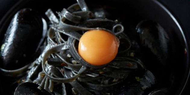 Squid ink fettucine pasta with mussels and egg yolk in a black pot