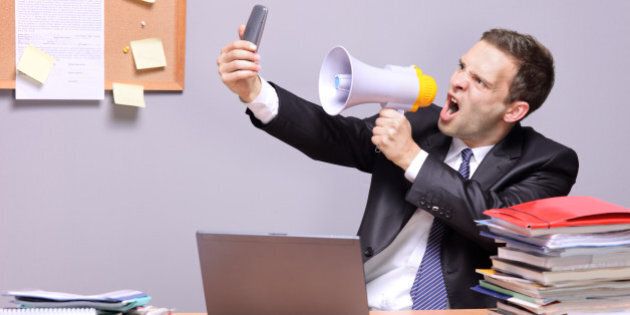 'Angry businessman in an office, shouting on a megaphone'