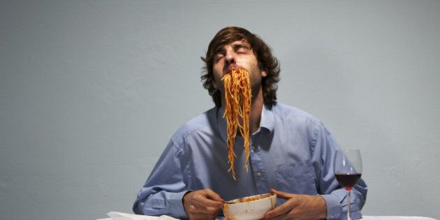 Man sitting at table, with spaghetti stuffed into mouth