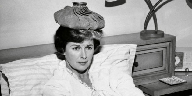 Mid adult woman reclining on the bed with an ice pack on her head