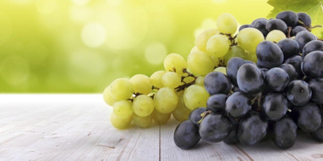 Wine collection: White and red grapes on table in vineyard. Blurred lights in background.