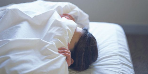 Woman lying in bed covering face with sheet