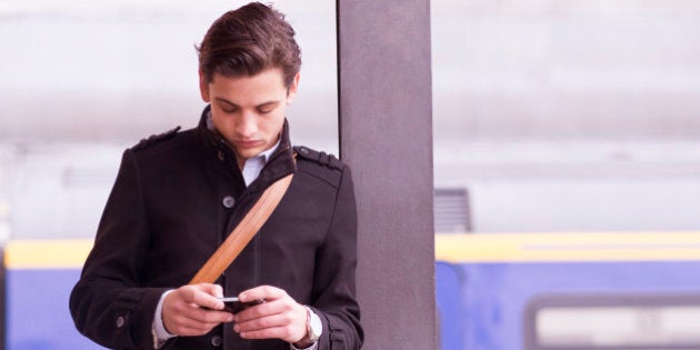 Man on train platform checks cell phone