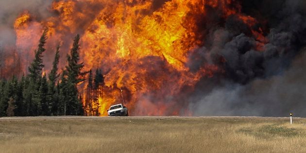 Smoke and flames from the wildfires erupt behind a car on the highway near Fort McMurray, Alberta, Canada, May 7, 2016. REUTERS/Mark Blinch TPX IMAGES OF THE DAY