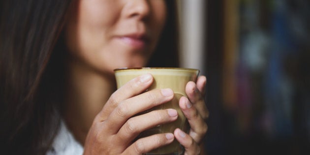 A young woman holds a cup of designer coffee in two hands in a coffee shop.