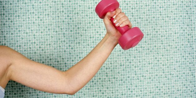 Young woman lifting dumbbell, against tiled wall, close-up