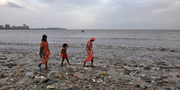 Ram Singh (L) and his relatives, dressed in traditional Hindu saffron-coloured clothes walk on a garbage-strewn beach against the backdrop of monsoon clouds on World Environment Day in Mumbai, June 5, 2012. According to the United Nations Environment Programme website, World Environment Day is celebrated annually on June 5 to raise global awareness and motivate action for environmental protection. REUTERS/Vivek Prakash (INDIA - Tags: ENVIRONMENT SOCIETY)