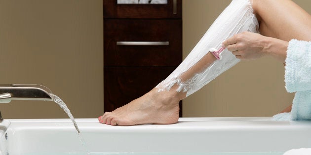 Caucasian woman shaving her legs at bathtub