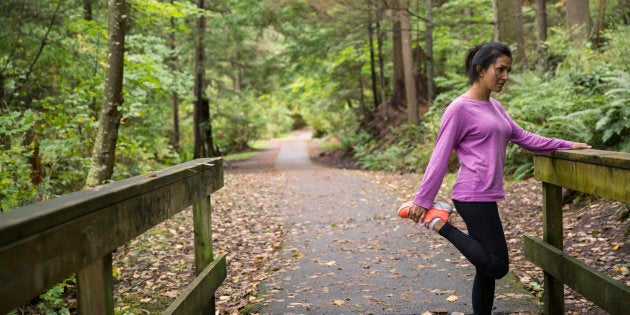 Woman stretching leg preparing for run in woods