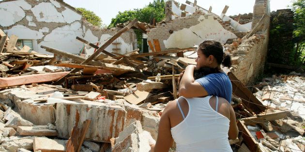 Women hug while standing next to a destroyed house.