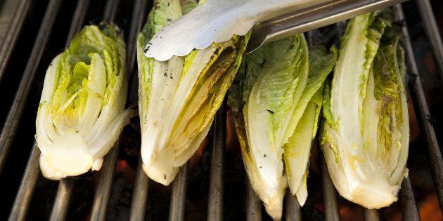 Tongs turning heads of romaine lettuce on grill