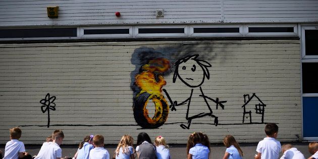 Reception class school children sit in a row as they draw a mural, attributed to graffiti artist Banksy, painted on the outside of a class room at the Bridge Farm Primary School in Bristol, Britain June 6, 2016. REUTERS/Dylan Martinez