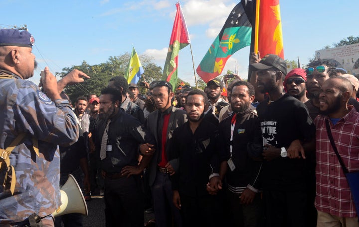 A Papua New Guinea police special services division officer (L) talks through a megaphone as students attempt to march from University of Papua New Guinea in Port Moresby, Papua New Guinea, June 8, 2016.