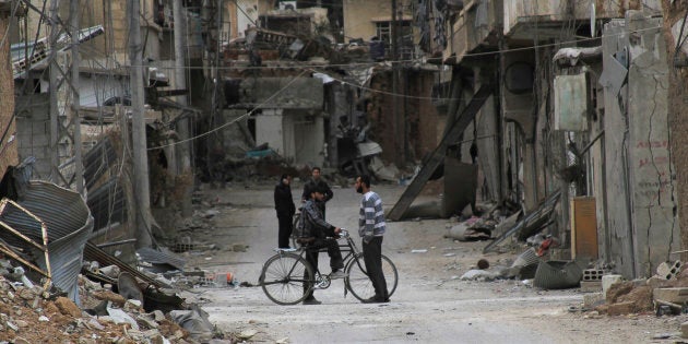 Men chat near buildings damaged by what activists said was shelling by forces loyal to Syria's President Bashar al-Assad in Daraya, near Damascus February 2, 2014. Picture taken February 2, 2014.REUTERS/Omar Abu Bakr (SYRIA - Tags: POLITICS CIVIL UNREST CONFLICT)