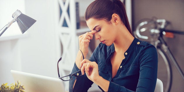 Frustrated young woman keeping eyes closed and massaging nose while sitting at her working place in office