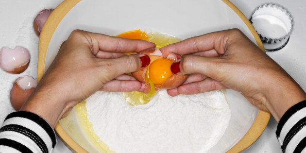 Feamle cracking egg into bowl with flour