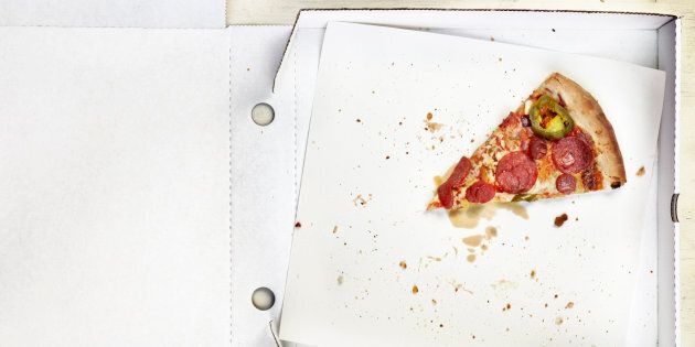 A single slice of pizza left in an open, white pizza box on a wooden table top