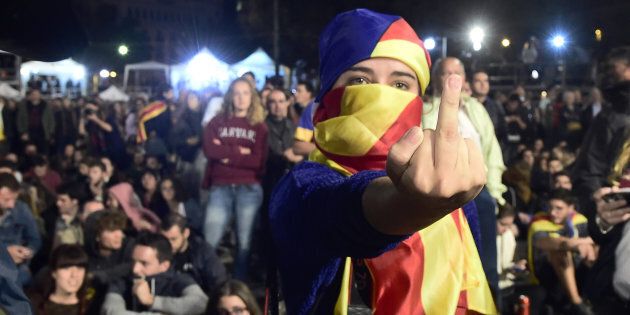 A woman, whose face is covered with a Catalan pro-independence flag, gestures as people sit on Plaza Catalunya square in Barcelona waiting for polls results after the closing of polling stations on October 1, 2017. / AFP PHOTO / JOSE JORDAN (Photo credit should read JOSE JORDAN/AFP/Getty Images)