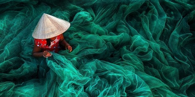 In a small village in southern Vietnam near Phan Rang a woman wearing a typical cone hat is creating a fishing net in their traditional manner The manufacturing of handmade nets is still a typical Vietnamese activity for women which they carry on while their husbands are out fishing