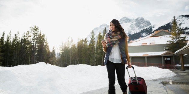 Woman pulling suitcase on sidewalk below mountains