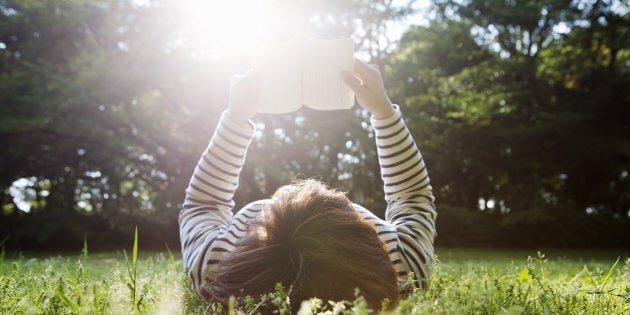 woman lying down on grass and reading a book.