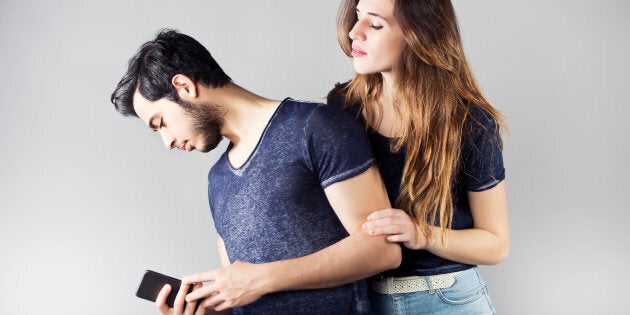 Young man with mobile phone and his girlfriend trying to see what he does behind him