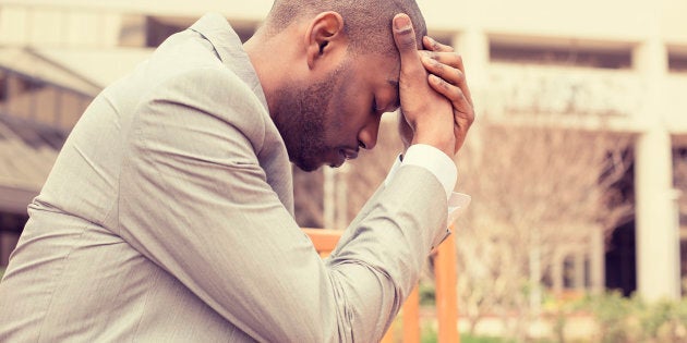 side profile stressed young businessman sitting outside corporate office holding head with hands looking down. Negative human emotion facial expression feelings.