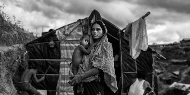 COX'S BAZAR, BANGLADESH - SEPTEMBER 27: A Rohingya refugee woman holds her child as she stands outside her shelter at the sprawling Balukali refugee camp on September 27, 2017 in Cox's Bazar, Bangladesh. More than half a million Rohingya refugees have flooded into Bangladesh to flee an offensive by Myanmar's military that the United Nations has called 'a textbook example of ethnic cleansing'. The refugee population is expected to swell further, with thousands more Rohingya Muslims said to be making the perilous journey on foot toward the border, or paying smugglers to take them across by water in wooden boats. Hundreds are known to have died trying to escape, and survivors arrive with horrifying accounts of villages burned, women raped, and scores killed in the 'clearance operations' by Myanmar's army and Buddhist mobs that were sparked by militant attacks on security posts in Rakhine state on August 25, 2017. What the Rohingya refugees flee to is a different kind of suffering in sprawling makeshift camps rife with fears of malnutrition, cholera, and other diseases. Aid organizations are struggling to keep pace with the scale of need and the staggering number of them - an estimated 60 percent - who are children arriving alone. Bangladesh, whose acceptance of the refugees has been praised by humanitarian officials for saving lives, has urged the creation of an internationally-recognized 'safe zone' where refugees can return, though Rohingya Muslims have long been persecuted in predominantly Buddhist Myanmar. World leaders are still debating how to confront the country and its de facto leader, Aung San Suu Kyi, a Nobel Peace Prize laureate who championed democracy, but now appears unable or unwilling to stop the army's brutal crackdown. (Photo by Kevin Frayer/Getty Images)