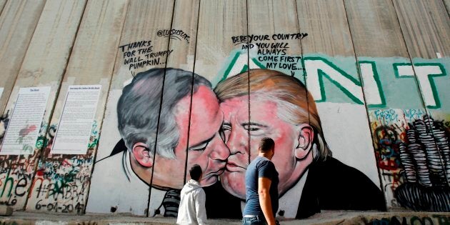 Palestinian men walk past a graffiti by street artist Lushsux.