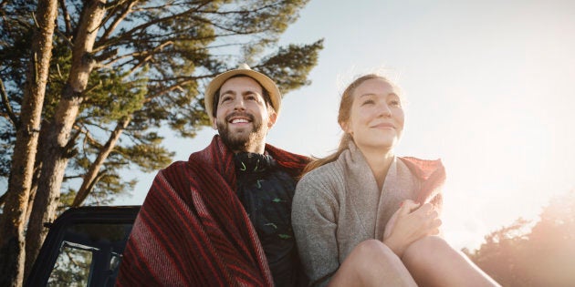 Happy wonderlust couple wrapped in blanket sitting on jeep against clear sky