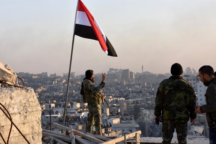 A Syrian government soldier gestures a v-sign under the Syrian national flag near a general view of eastern Aleppo after they took control of al-Sakhour neigbourhood in Aleppo.